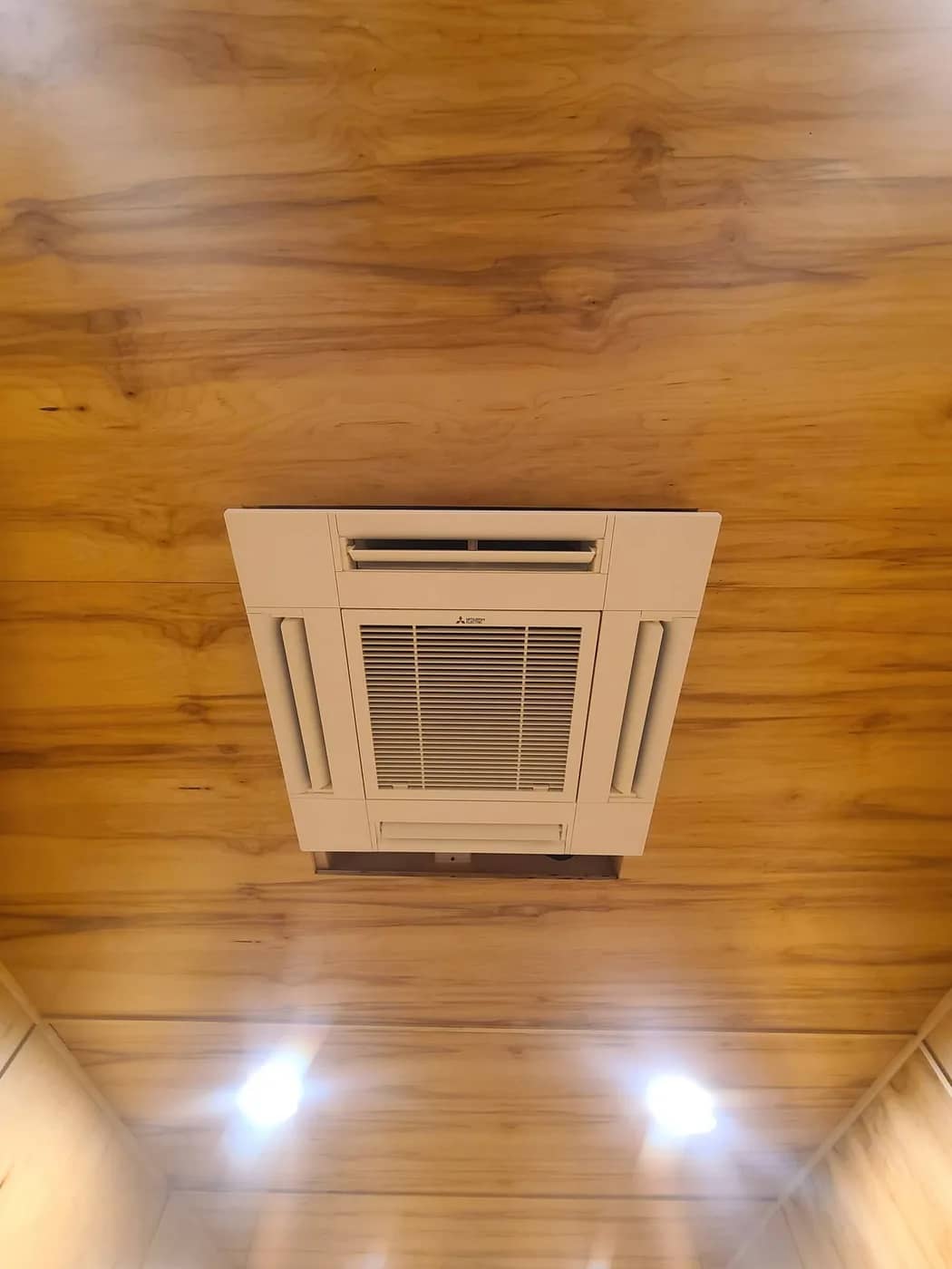 Mitsubishi four-way ceiling cassette heat pump head recessed into a wood-panelled ceiling
