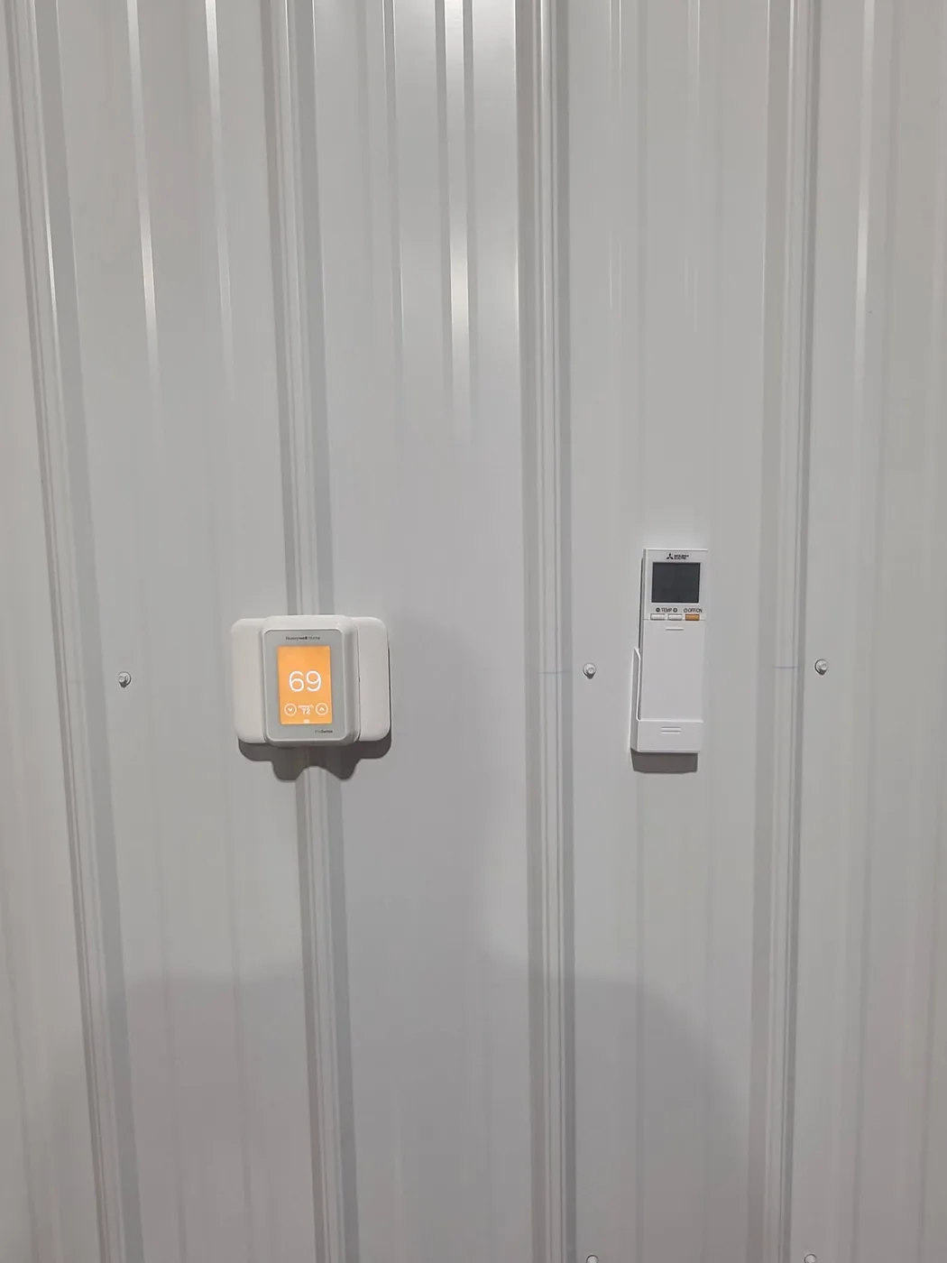 Honeywell Home thermostat reading 69 degrees next to a wall-mounted Mitsubishi heat pump remote controller